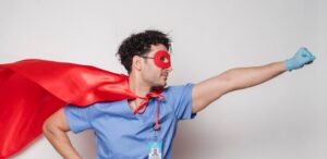 Male healthcare worker wearing a red cape and mask poses as a superhero. Studio shot.